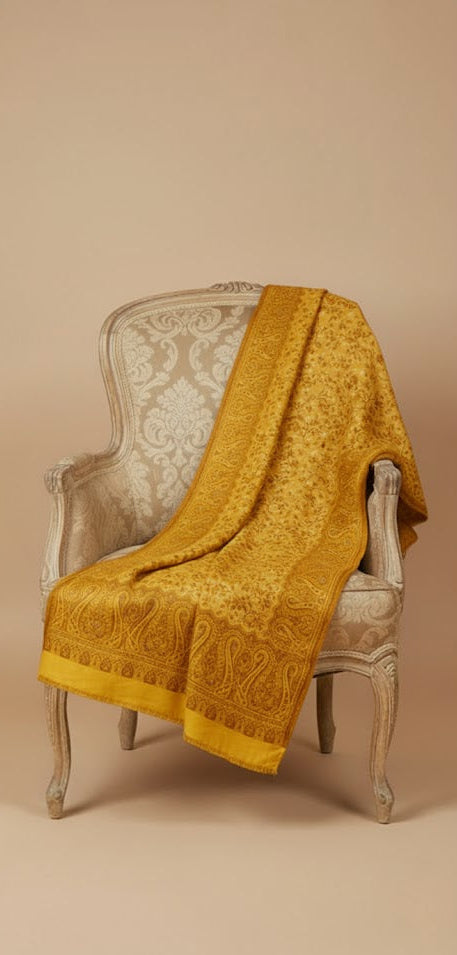 Yellow textured shawl draped over a decorative chair against a beige background