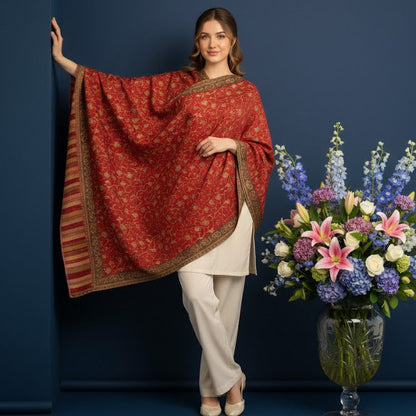 Woman in a red patterned shawl and white outfit standing next to a vase of flowers against a blue background