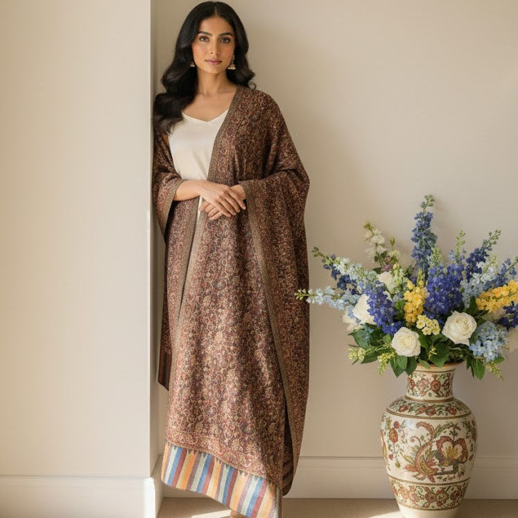 Woman wearing a brown patterned shawl over a white top, standing next to a vase with flowers.