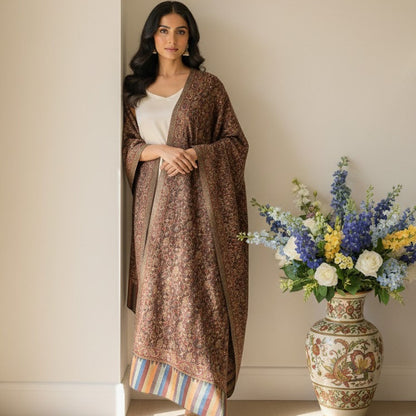 Woman wearing a brown patterned shawl over a white top, standing next to a vase with flowers.