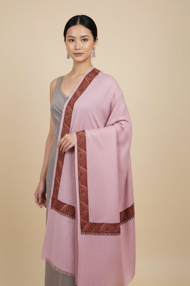 Woman wearing a luxury pashmina kashmiri sozni hand embroidered border dusty pink shawl  with brown trim on a beige background
