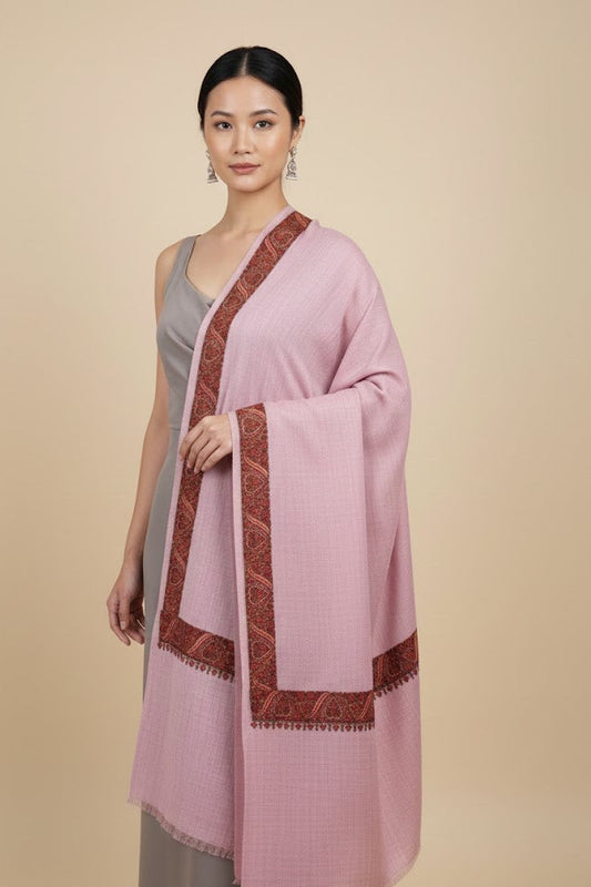 Woman wearing a luxury pashmina kashmiri sozni hand embroidered border dusty pink shawl  with brown trim on a beige background