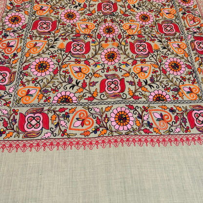 A rectangular embroidered table runner laid out on a dark marble dining table with brown upholstered chairs. The runner features a dense floral and geometric pattern in red, orange, yellow, green, and pink on a light sage green base, with a solid sage green border at the bottom.