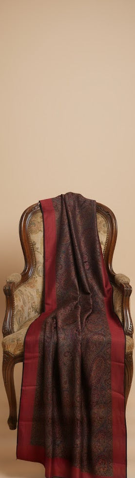 Brown and red patterned stole draped over a wooden chair against a beige wall.