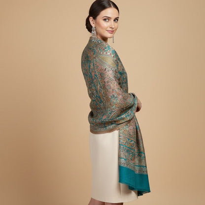 Woman wearing a patterned deep teal blue patterned jamawar kani pure wool shawl over a plain dress on a beige background