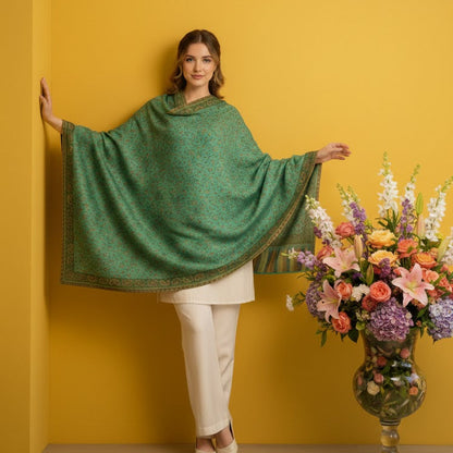 Woman wearing a green shawl against a yellow wall with a floral arrangement.