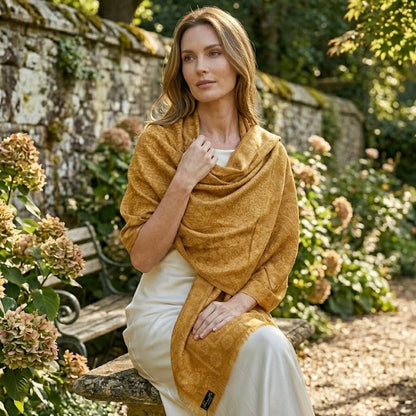 Woman sitting outdoors wearing a mustard yellow shawl and white dress.