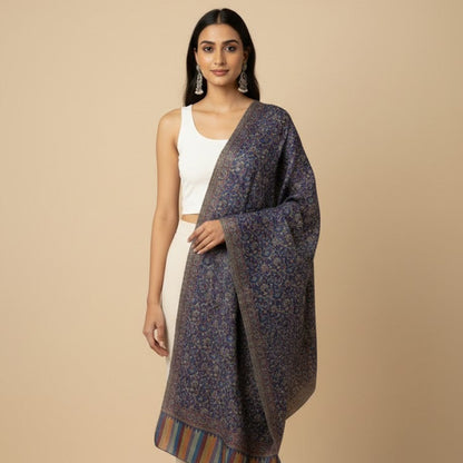 Woman wearing a patterned shawl over a plain top and pants on a beige background