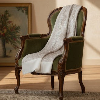 Vintage armchair with a white shawl draped over it in a room with a painting on the wall.