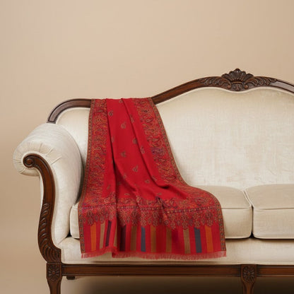 Red patterned blanket draped over a white sofa with a beige background
