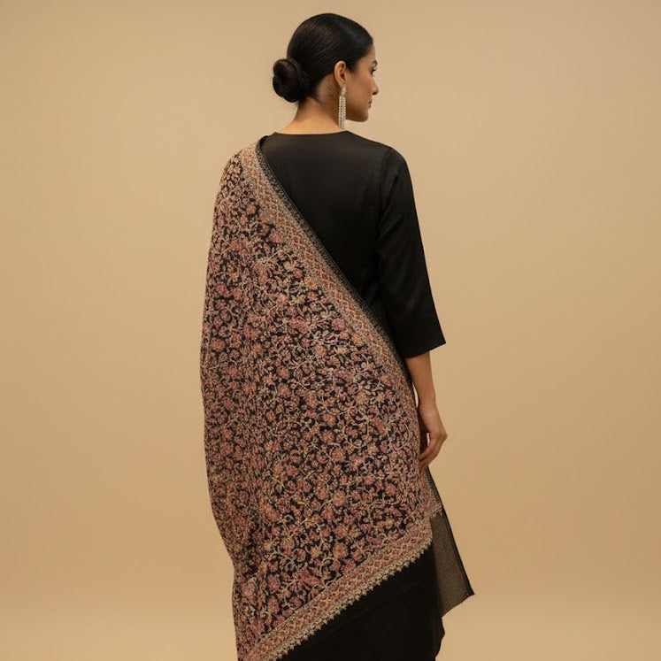 Woman wearing a patterned shawl over a black dress on a beige background