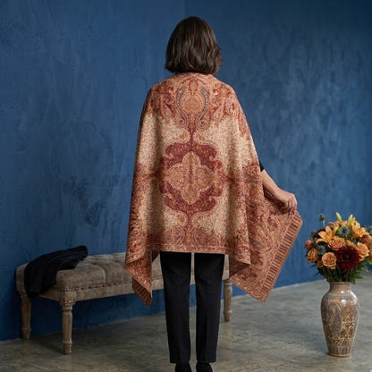 Woman wearing a patterned cape in a room with a blue wall, bench, and vase with flowers.