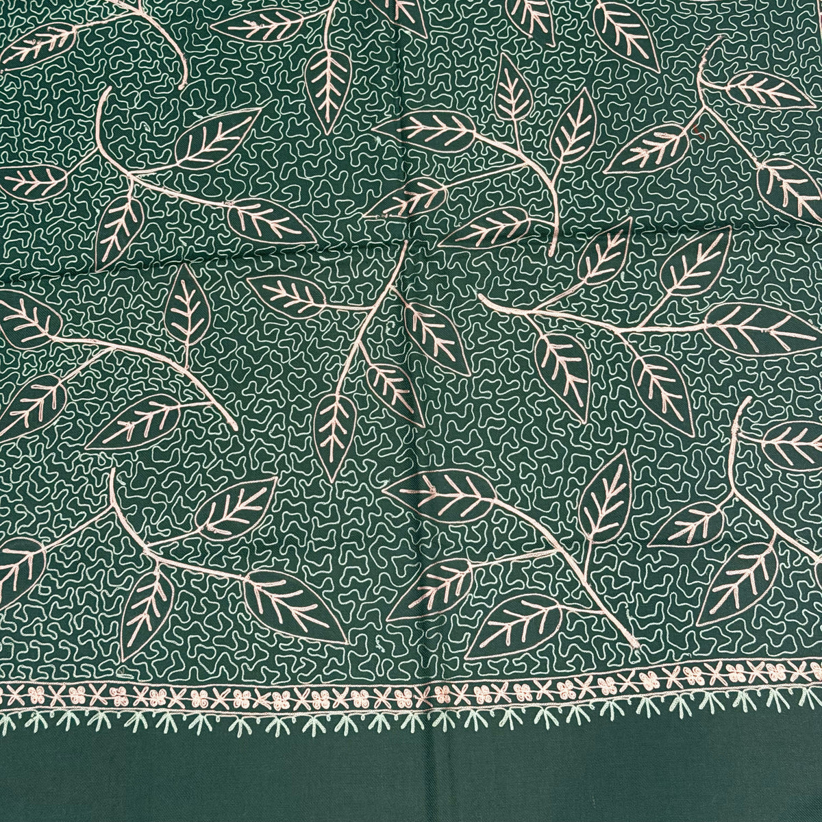 A close-up of a dark green fabric with a white hand-block printed leaf pattern and a decorative border along the right edge.