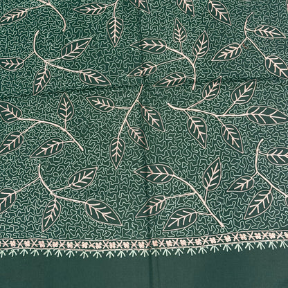A close-up of a dark green fabric with a white hand-block printed leaf pattern and a decorative border along the right edge.