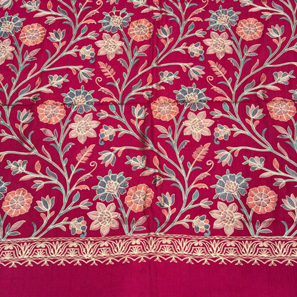 A close-up of a rich magenta pink fabric featuring an intricate floral and vine pattern in beige, light blue, and coral, with a decorative embroidered border on the right side.