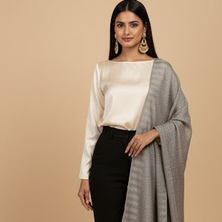 Woman wearing a white top, black pants, and a gray shawl on a beige background