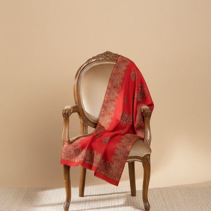 Red patterned scarf draped over a wooden chair against a beige wall.