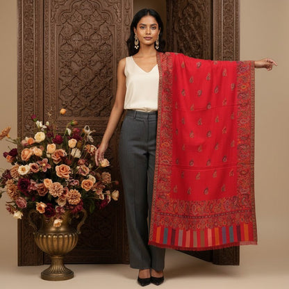 Woman holding a red scarf in front of an ornate wooden door with flowers on a table.