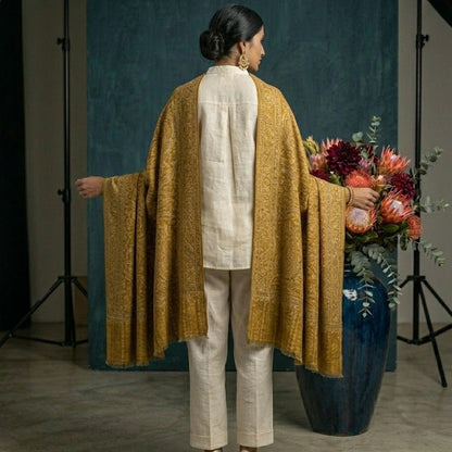 Person wearing a mustard yellow garment with a white outfit, standing in front of a blue backdrop with floral arrangements.