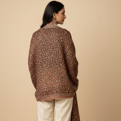 Woman wearing a patterned long jacket and white pants on a beige background