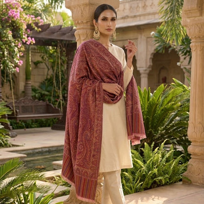 A woman models a traditional Indian outfit consisting of a cream kurta, matching trousers, and a rust-red patterned dupatta, set against an outdoor courtyard with stone pillars and lush green plants.