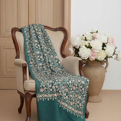 Teal floral-patterned blanket draped over a chair with a vase of flowers in the background.