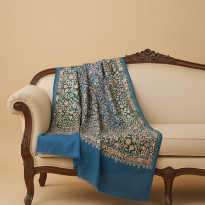Decorative blue and green patterned throw blanket draped over a beige sofa against a beige wall.