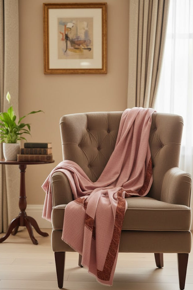 Beige armchair with a luxury pashmina kashmiri sozni hand embroidered border dusty pink shawl draped over it in a cozy living room setting.