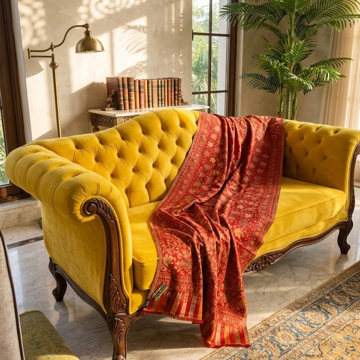 Yellow velvet sofa with a red blanket in a sunlit room with a plant and books.