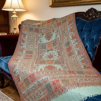 A large patterned wool throw blanket with a mint green base and intricate red, blue, and beige geometric designs, draped over a dark blue velvet sofa in a living room setting.