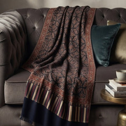 A dark brown and navy patterned throw blanket with striped borders is draped over a tufted gray sofa in a styled living room setting.