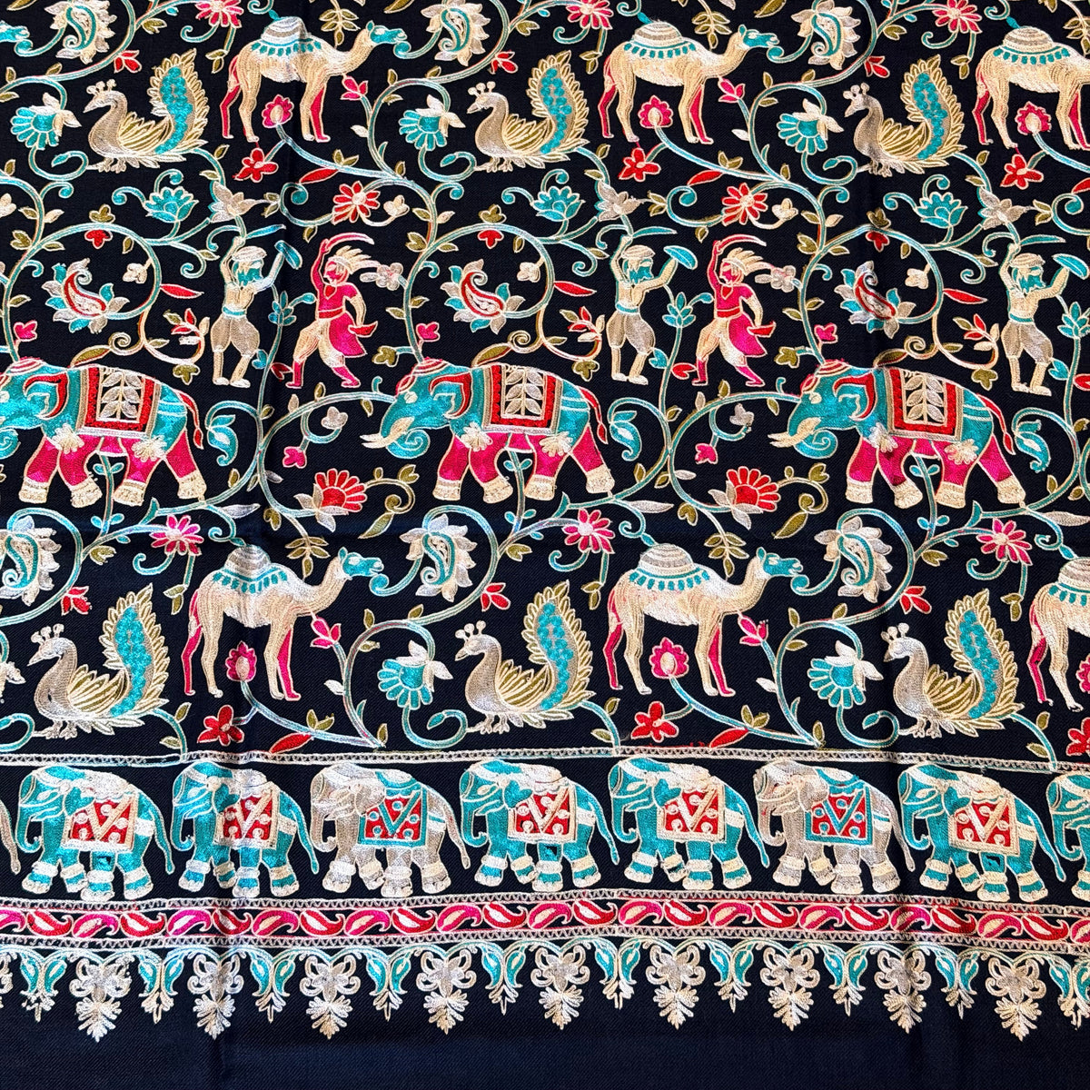A close-up of a black embroidered textile featuring intricate floral vines, birds, and a decorative border in red, turquoise, beige, and gold thread.
