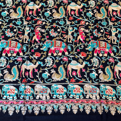 A close-up of a black embroidered textile featuring intricate floral vines, birds, and a decorative border in red, turquoise, beige, and gold thread.