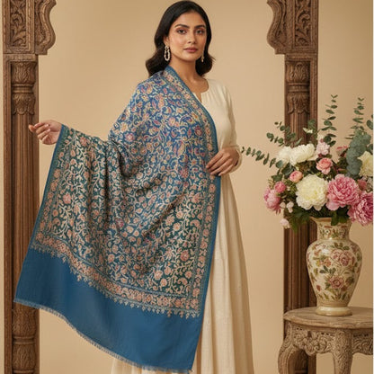 Woman wearing a floral shawl over a white outfit, standing in front of an ornate wooden frame and floral arrangement.