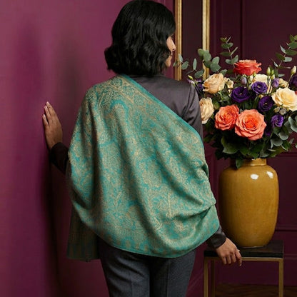 Person wearing a teal patterned shawl standing next to a vase of flowers against a purple wall.