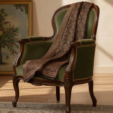 Green armchair with a brown patterned shawl in a room with a painting on the wall.
