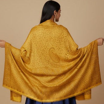 Woman wearing a yellow shawl over a blue dress on a beige background