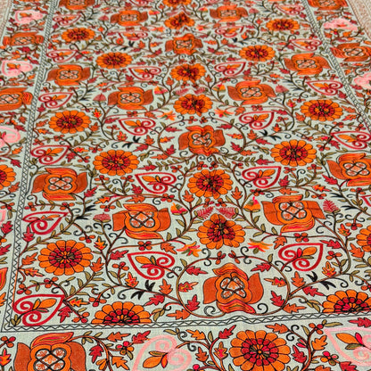 A rectangular table runner with a light mint green base and an intricate orange, red, and green floral pattern, laid out on a dark marble kitchen island.