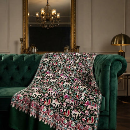 A dark green velvet throw blanket draped over a matching green tufted armchair in a classic living room setting, featuring a highly detailed multicolor embroidered pattern of horses, lions, and floral motifs.