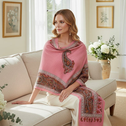 Woman sitting on a couch wearing a pink shawl with paisley patterns in a bright living room.