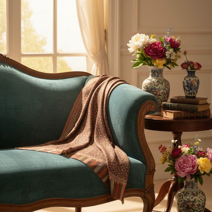 Vintage-style teal sofa with wooden armrests in a sunlit room with floral arrangements and books.