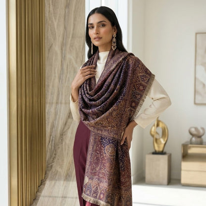 A woman models a luxurious patterned shawl draped over her shoulders. The shawl features an intricate, dense traditional pattern in deep purple, burgundy, and gold, with a fringed edge.