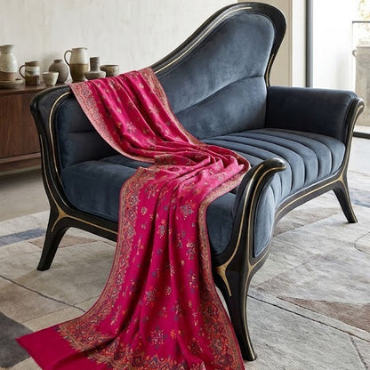 A vibrant magenta pink patterned silk scarf draped over a dark blue velvet chaise lounge in a modern, neutral-toned room.