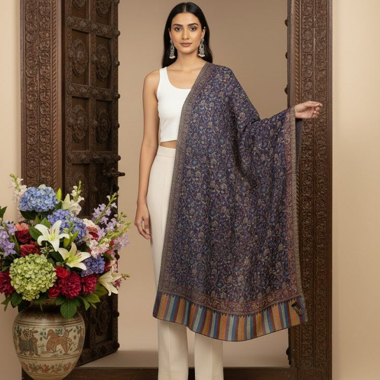 Woman in a white outfit with a dark floral shawl standing in front of an ornate wooden door with flowers on a table.