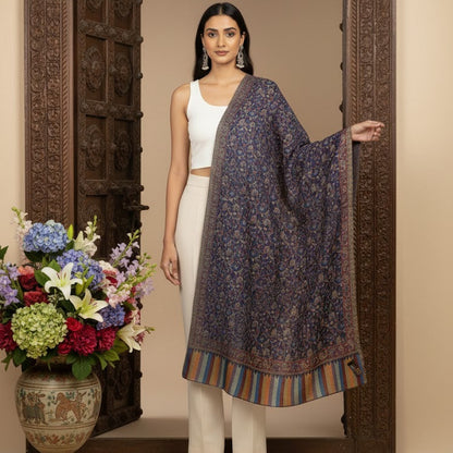 Woman in a white outfit with a dark floral shawl standing in front of an ornate wooden door with flowers on a table.