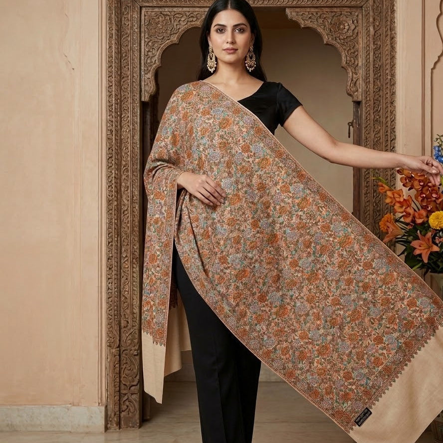 Woman holding a floral-patterned shawl in a decorative setting with a vase of flowers.