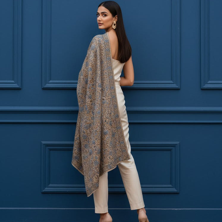 Beautiful Sozni embroidery shawl in beige with blue embroidery draped over a female model standing in a beautiful room