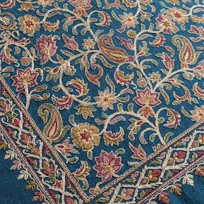 A close-up of a blue patterned textile with an intricate floral and paisley design in pink, gold, and cream tones.