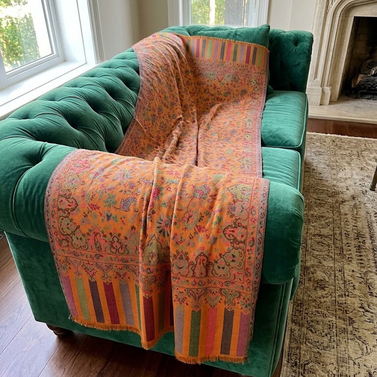 A vibrant orange and multicolor patterned throw blanket draped over a green velvet sofa in a living room setting.