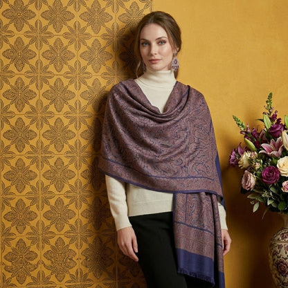 Woman wearing a patterned shawl against a decorative wall with a vase of flowers.